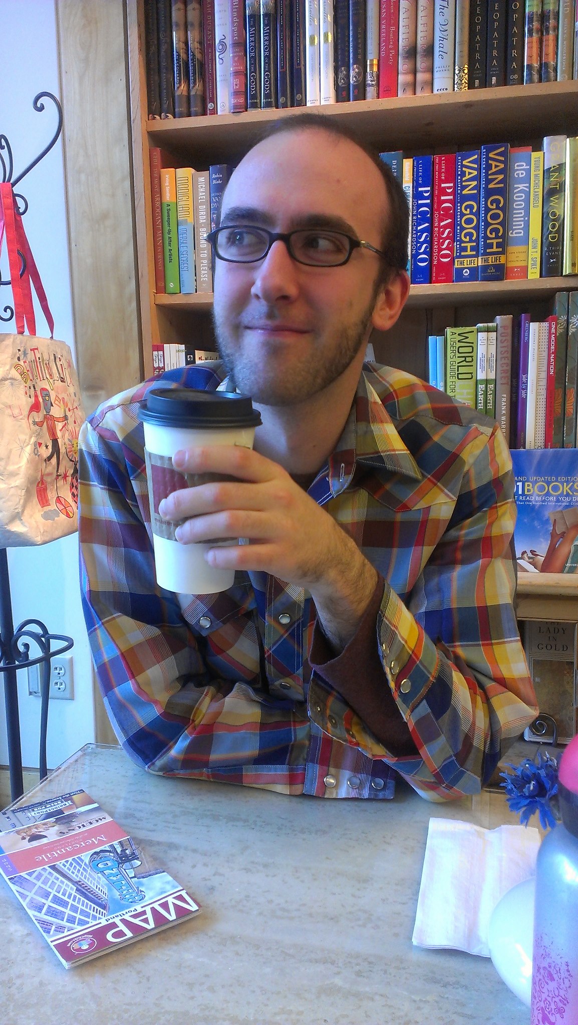 Michael sitting in front of a colorful bookshelf, holding a coffee cup and grinning off to the left.